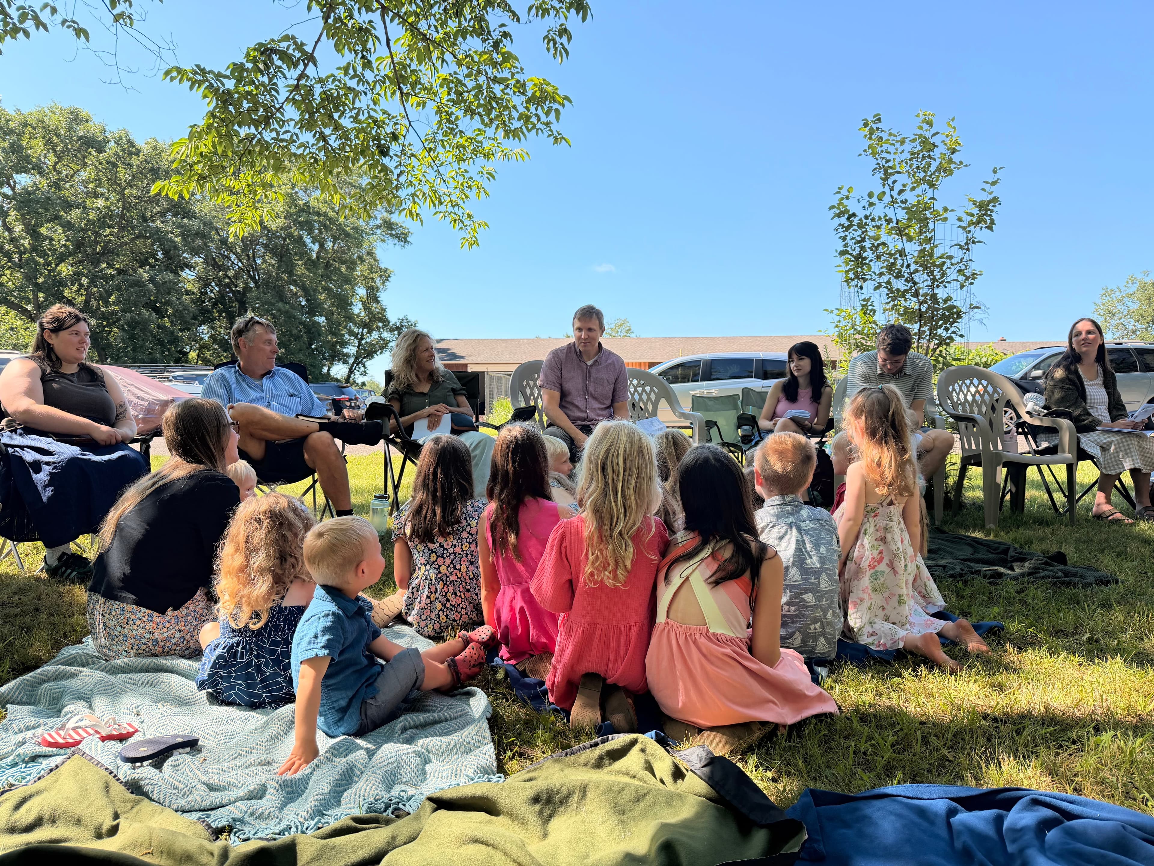 Children and adults gathered outdoors for teaching and conversation